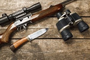Hunting rifle and binoculars on dark wooden background, close up